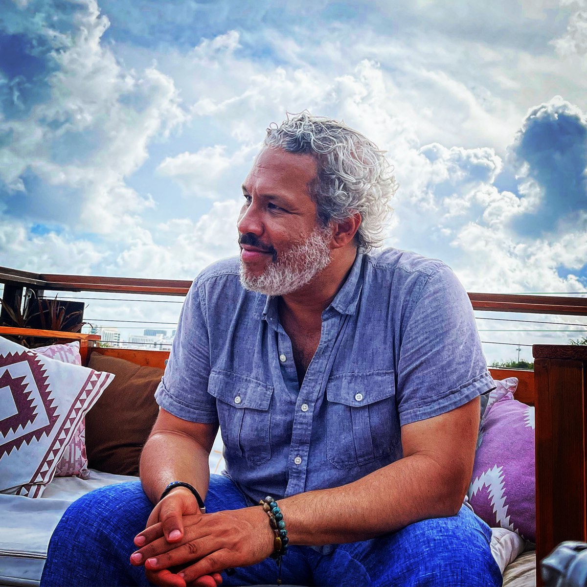 Khary Lazarre-White seated outdoors on a rooftop terrace, looking off to one side
