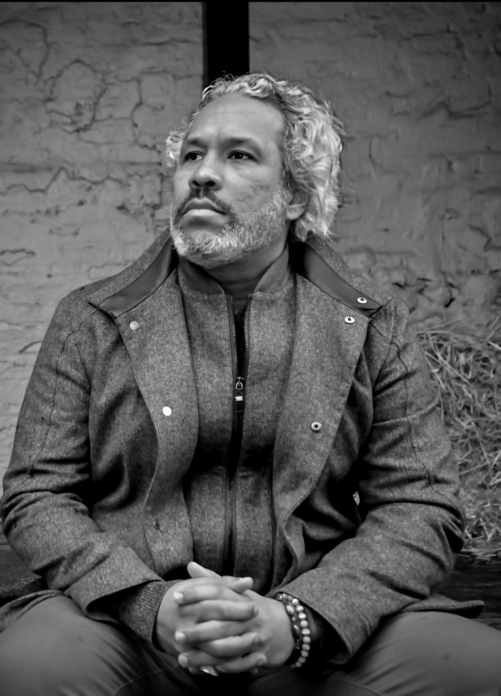 Khary Lazarre-White seated against a brick wall, looking away from the camera